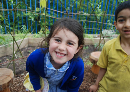 girl and boy in school uniforms smile at camera as part of school growing project in Manchester