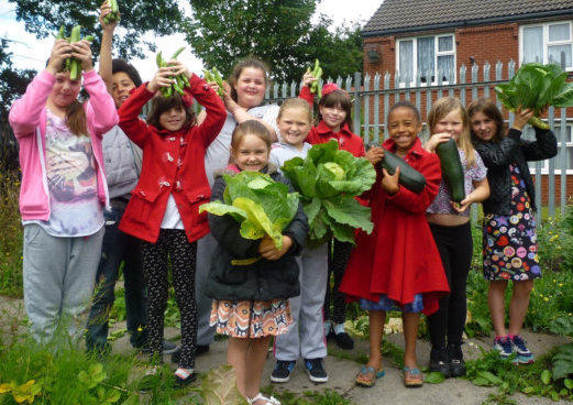 growing group with children and adults hold up produce they have grown