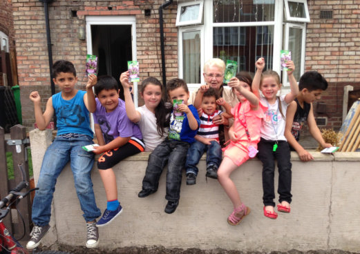 group of children sat holding up seed packets as part of commuity growing project